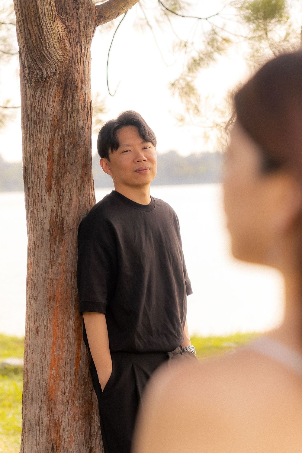 A couple shares a gentle moment beside a tree near a lake during golden hour.