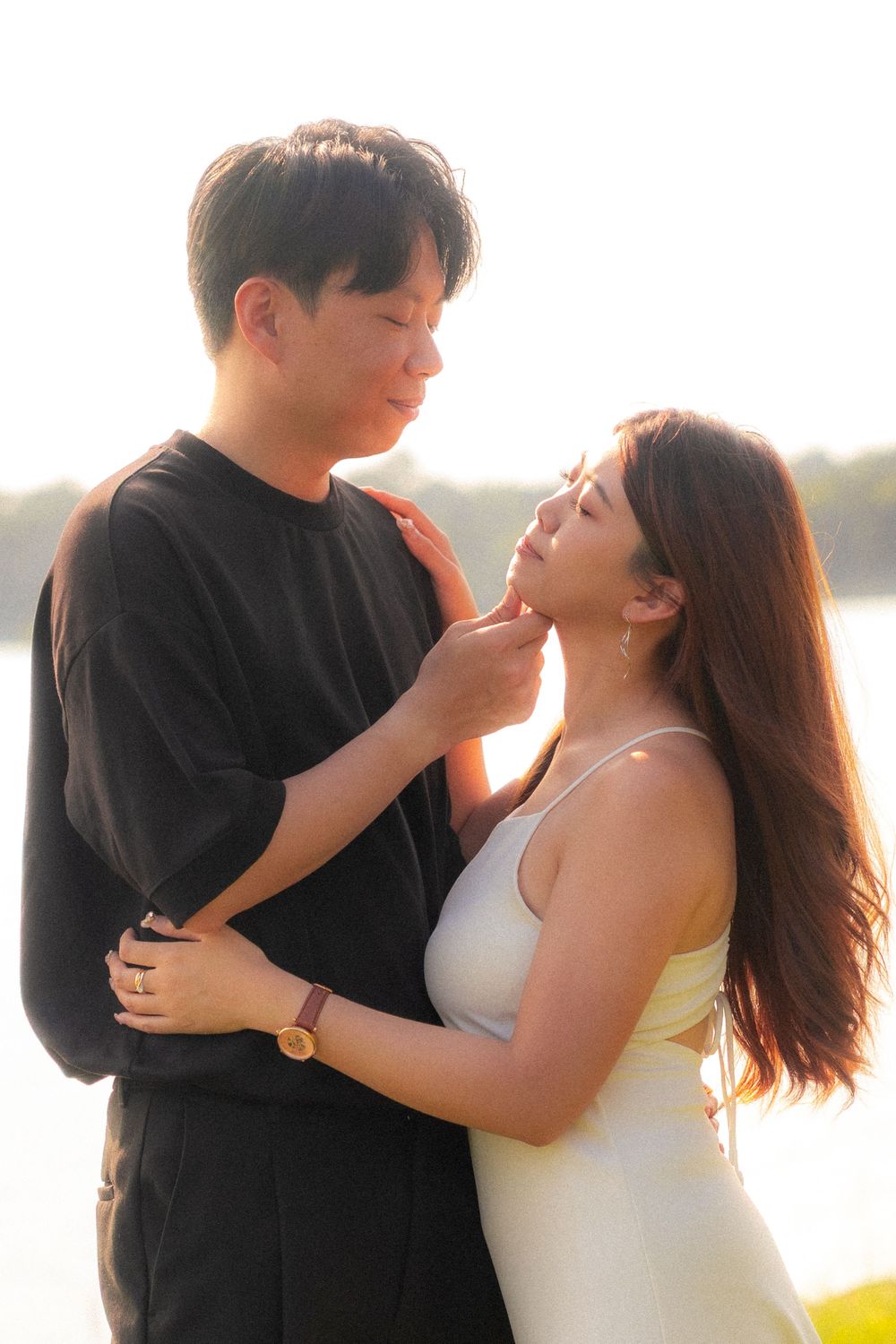 A romantic couple embraces in soft sunlight near a waterfront setting.