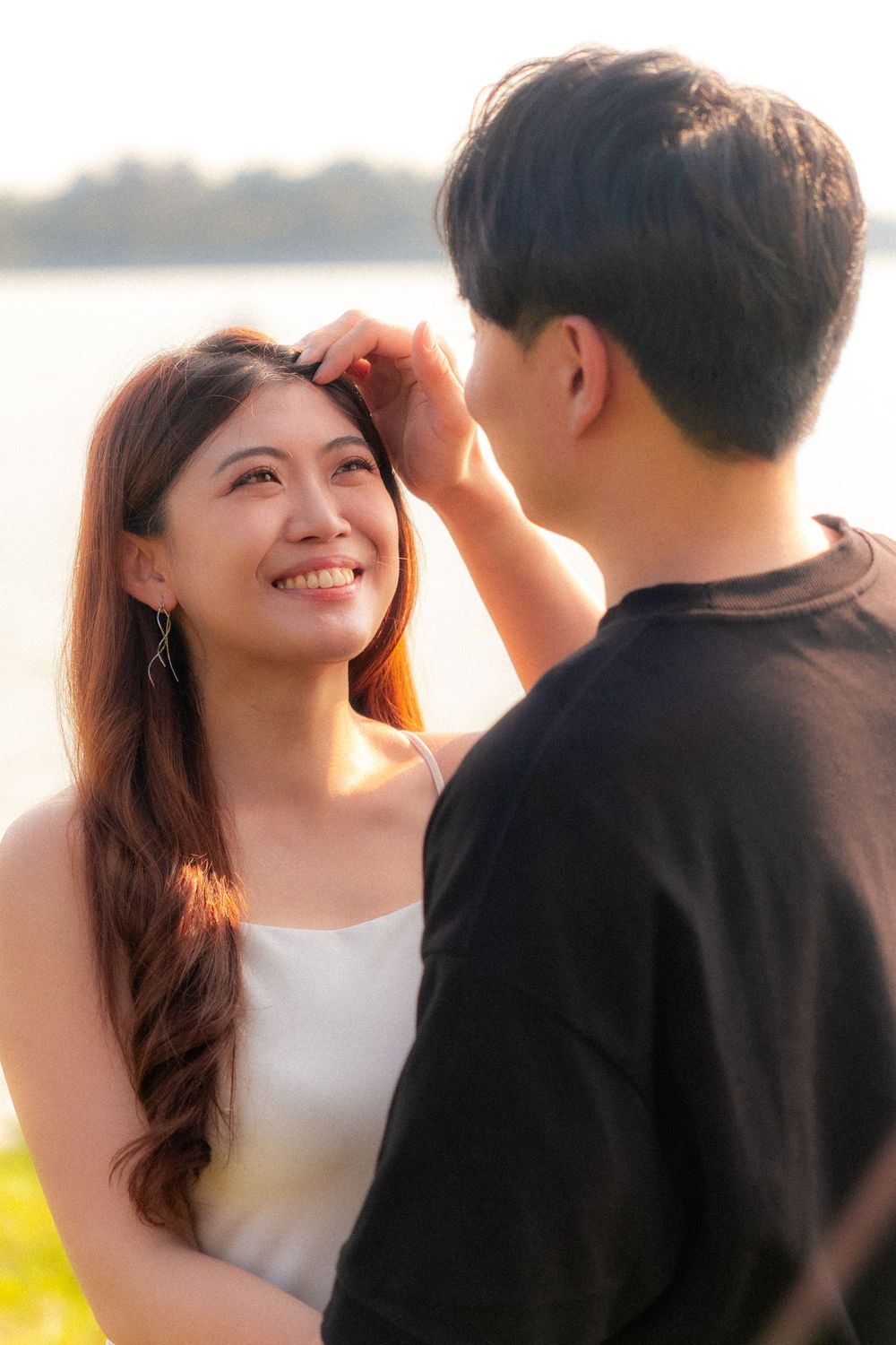 A romantic sunset moment between a couple with golden sunlight shining through the trees by the water.