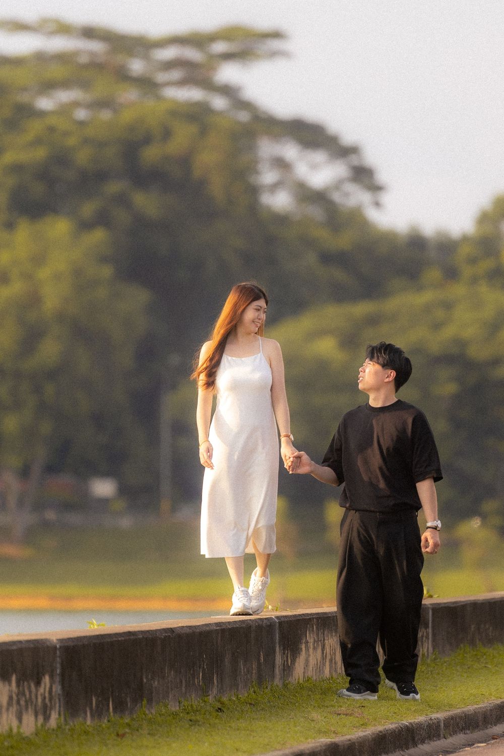 A couple standing on a stone ledge together by a peaceful lake surrounded by trees.