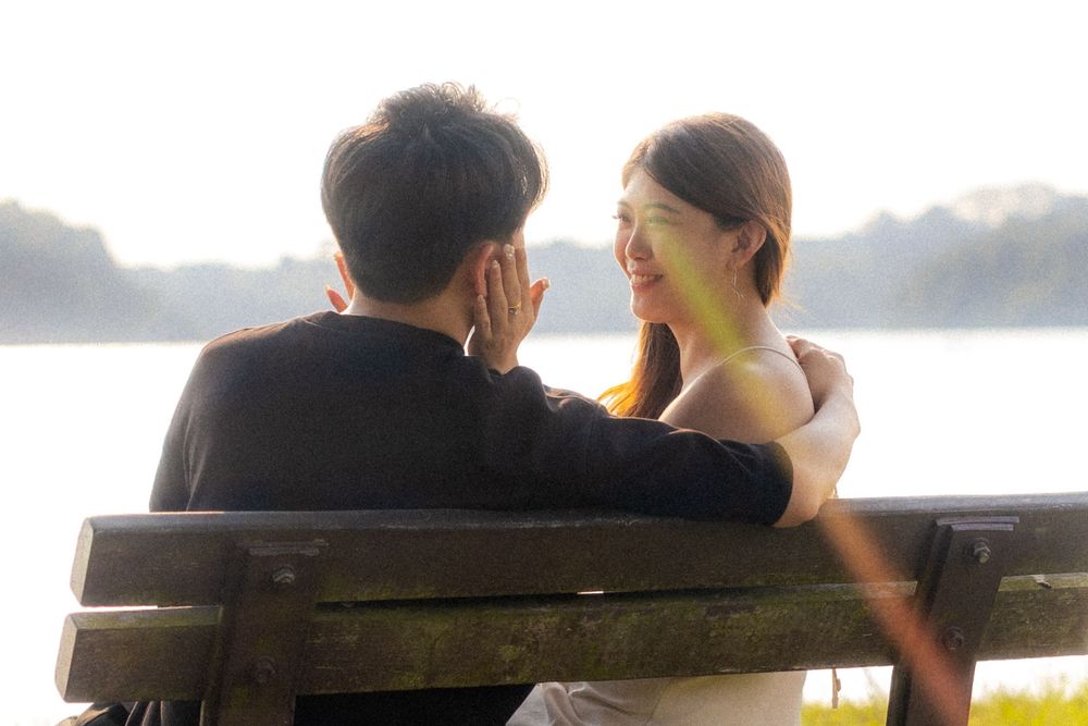 Couple sharing an intimate moment together on a wooden bench by the water during sunset.