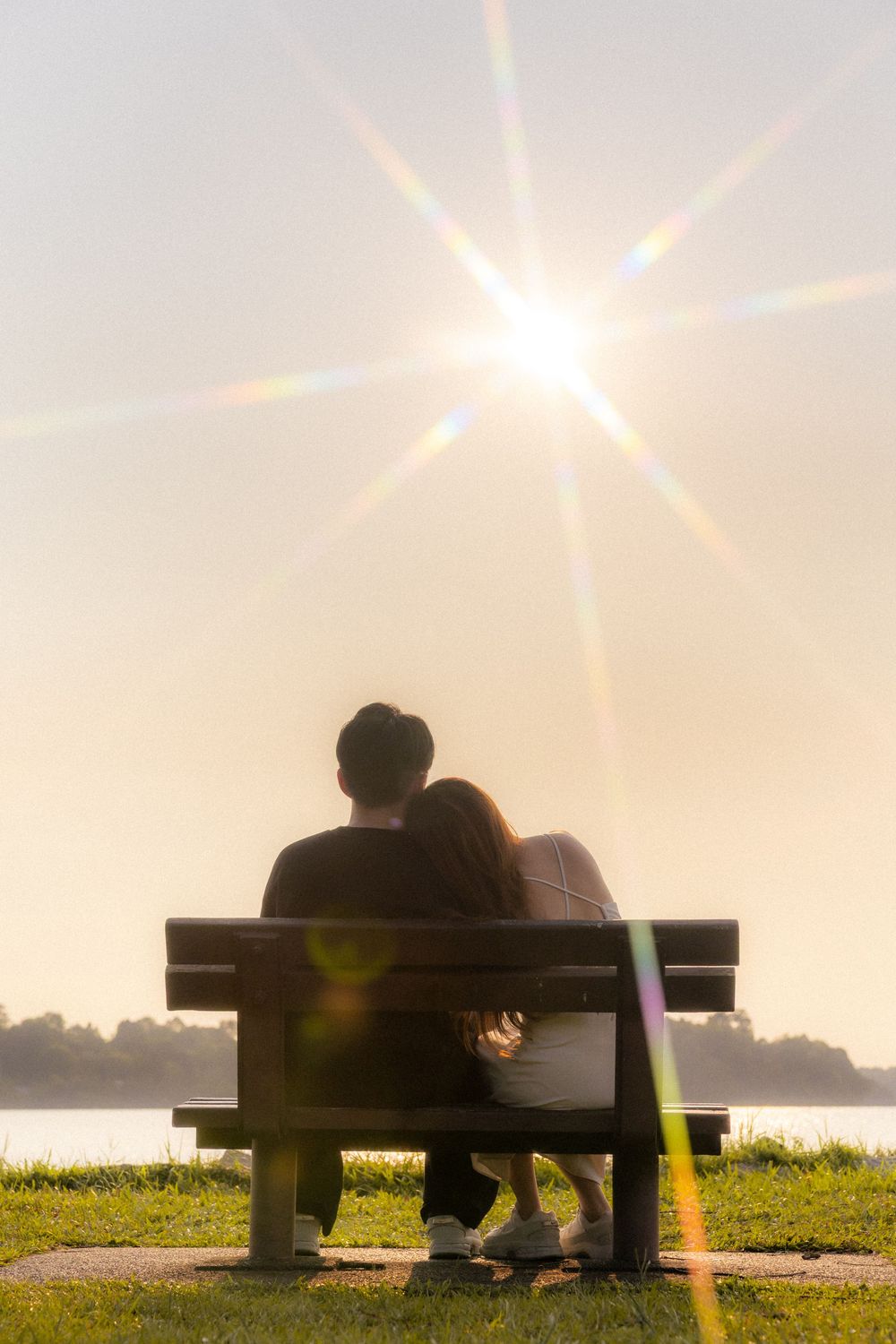 Couple sitting on park bench with dramatic sunburst effect in background.