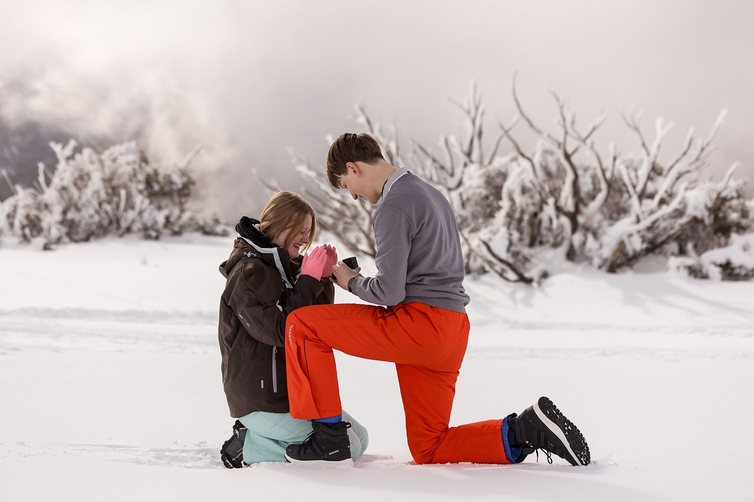 A winter marriage proposal scene with snowy mountain peaks in the background as a couple shares a special moment at Falls Creek Resort.