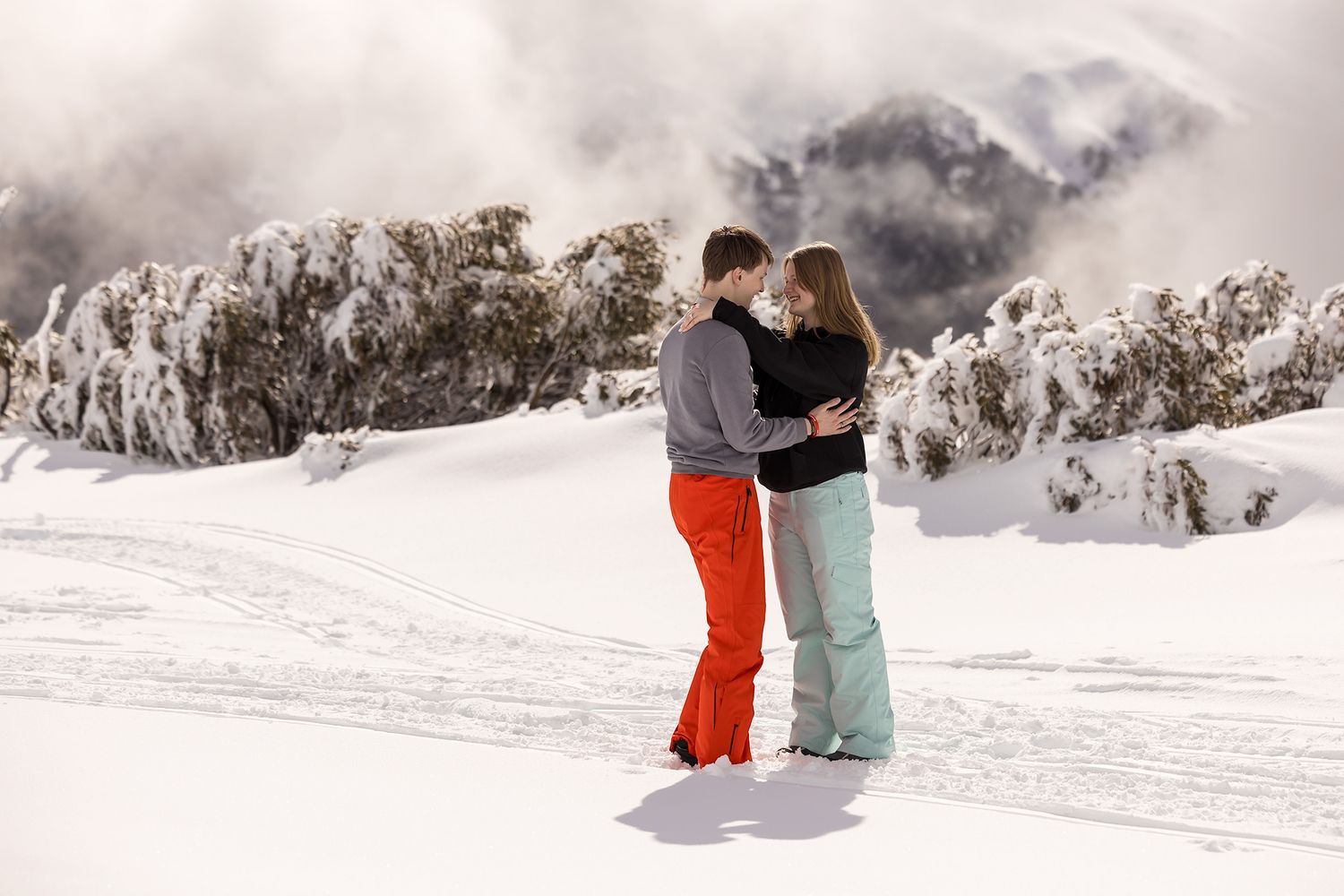 A newly Engaged couple hugging on a snowy mountain slope during a winter day with cloudy skies in the background at Falls Creek.