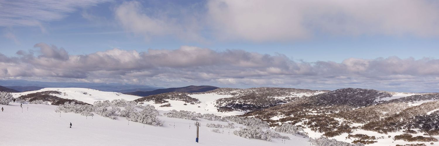 Scenic panoramic view of snow-covered mountains and ski slopes at Falls Creek Resort under a partly cloudy sky Looking towards Rocky Valley.