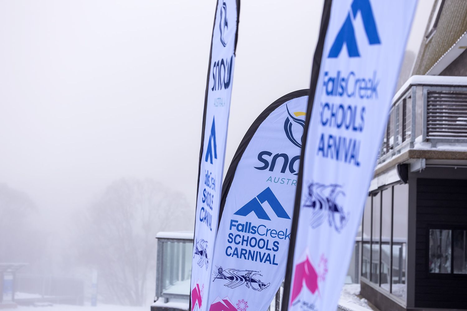 Blue and white banners with the Snow Falls Creek logo displayed along a building exterior.