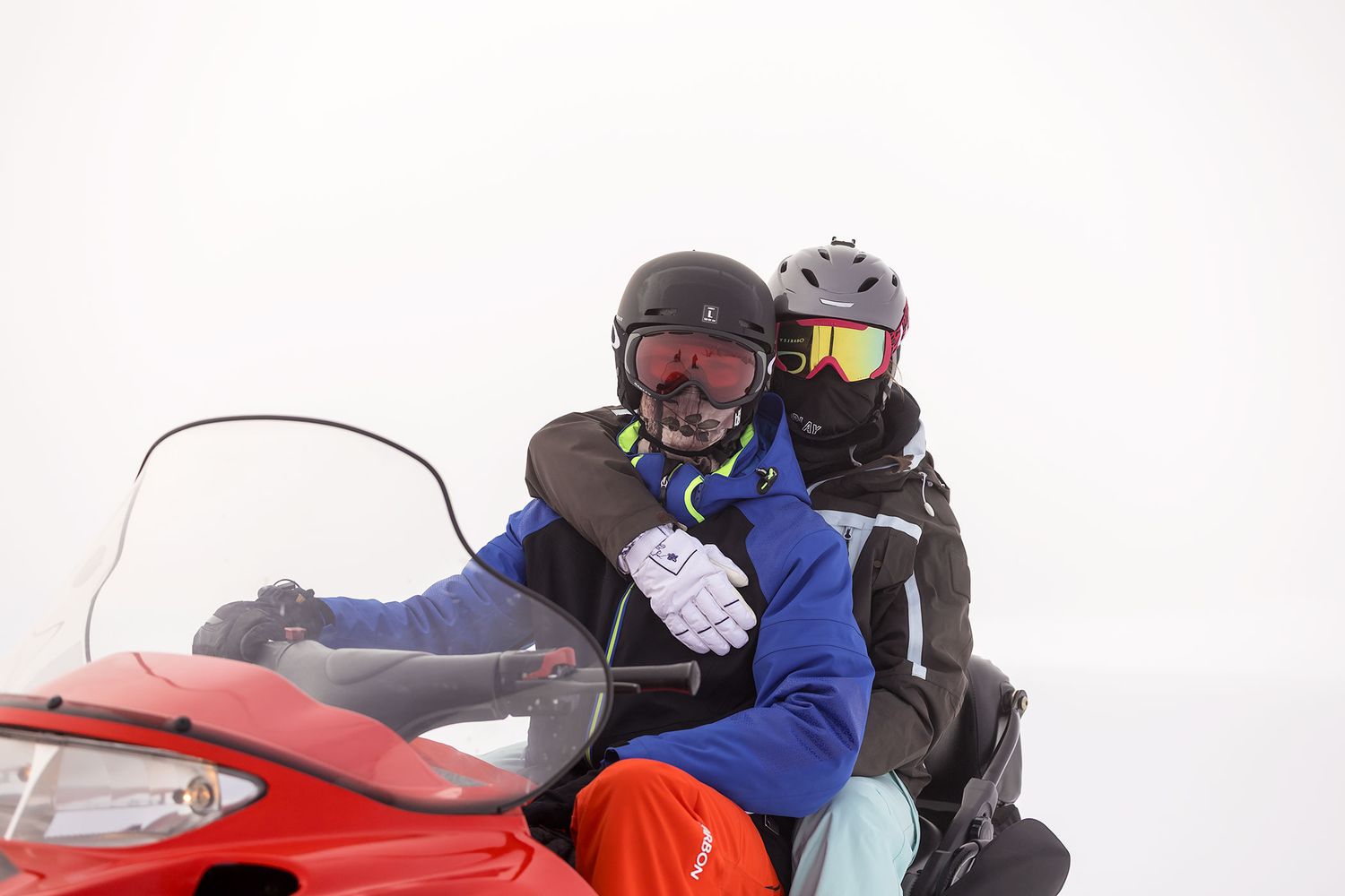 People riding snowmobiles through a snowy winter landscape with mountains visible through the fog in the background at Falls Creek.
