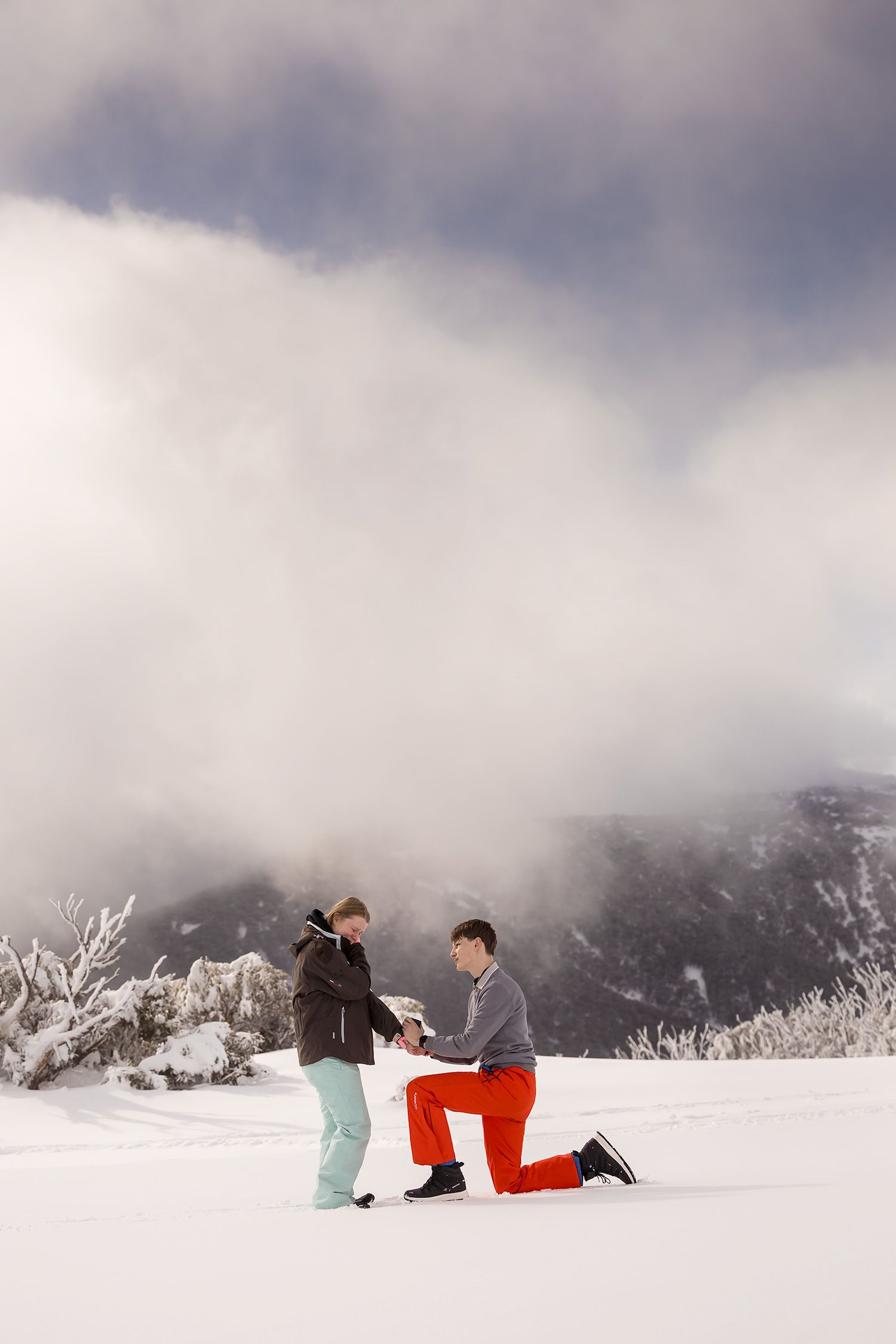 A winter marriage proposal scene with snowy mountain peaks in the background as a couple shares a special moment at Falls Creek Resort.