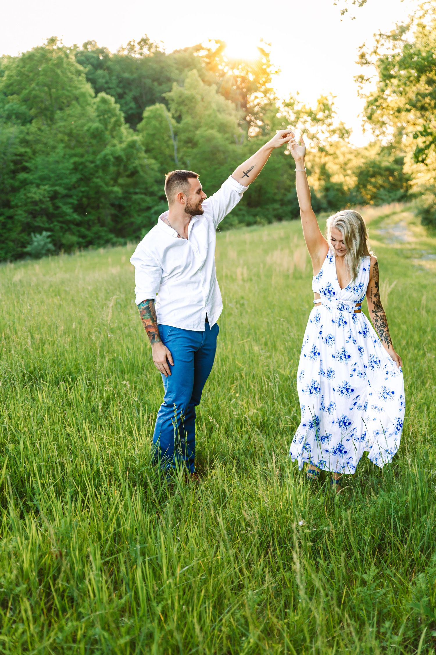 Couple in white and blue outfits dancing playfully in a sunlit meadow.