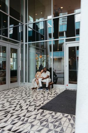 Modern office building entrance with geometric patterned floor tiles and glass walls shows people waiting in chairs.