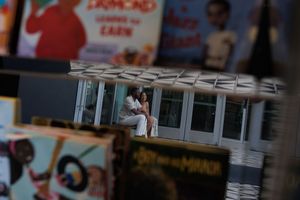 A figure sits in a miniature architectural model with small windows and a white overhang.