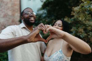 Two people making a heart shape with their hands together outdoors.