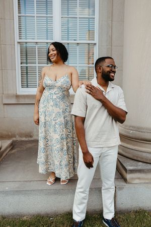 A couple enjoying a candid moment together outside a white building, wearing coordinated outfits of white and blue.