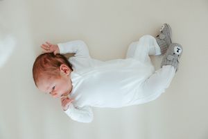 Baby sleeping peacefully on white blanket wearing soft white sleepwear and plush bunny slippers.