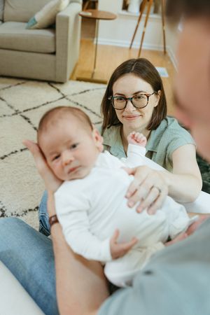 A series of four photos showing a baby in white clothing being held and cuddled while resting on a carpeted floor.
