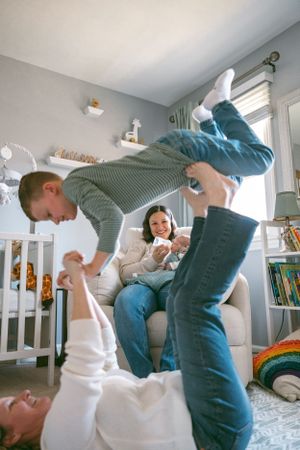 Family playing and laughing together in a cozy nursery room with natural light streaming through the windows.
