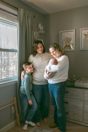 A cozy family moment in a nursery room with soft natural light coming through the window, decorated with neutral tones and artwork.