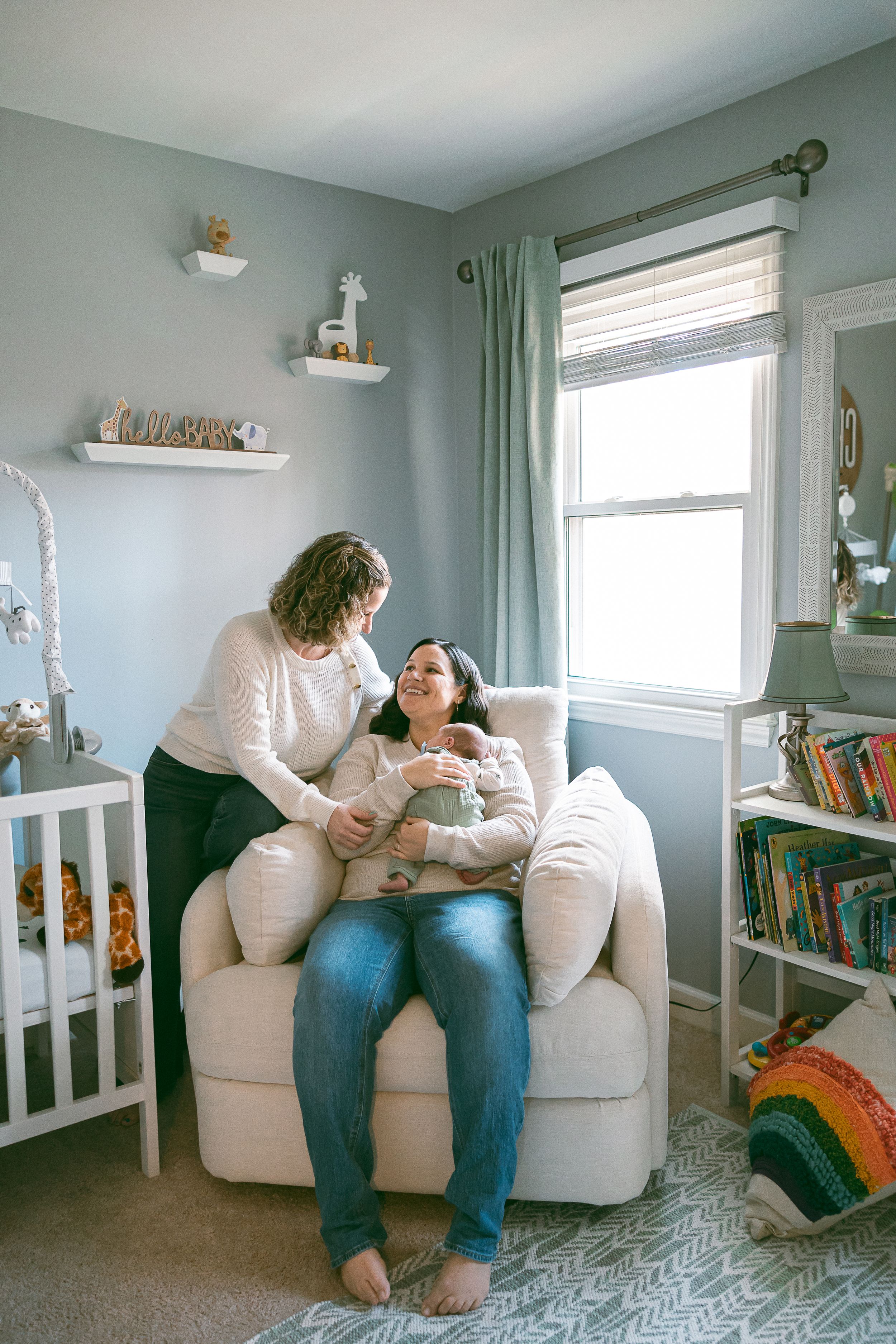 A cozy nursery room with pale green walls, floating shelves, a white crib, and a comfortable armchair near a bright window.