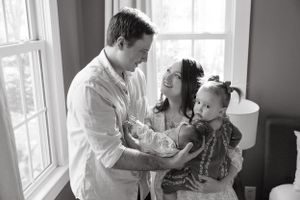A black and white photograph of a family sharing a tender moment together by a window.