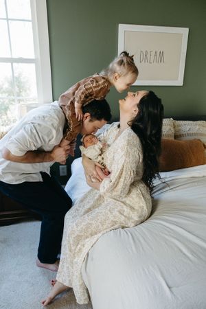 A tender family moment shared on a cozy bed next to a wall with a 'DREAM' frame in a green-painted room.