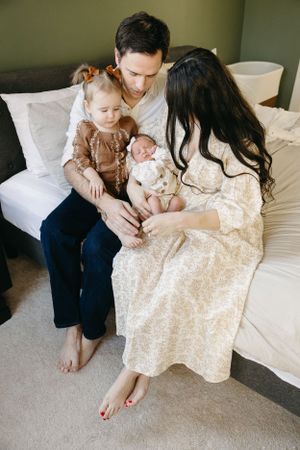 A family sits together on a couch, with a toddler and newborn baby, sharing an intimate moment at home.