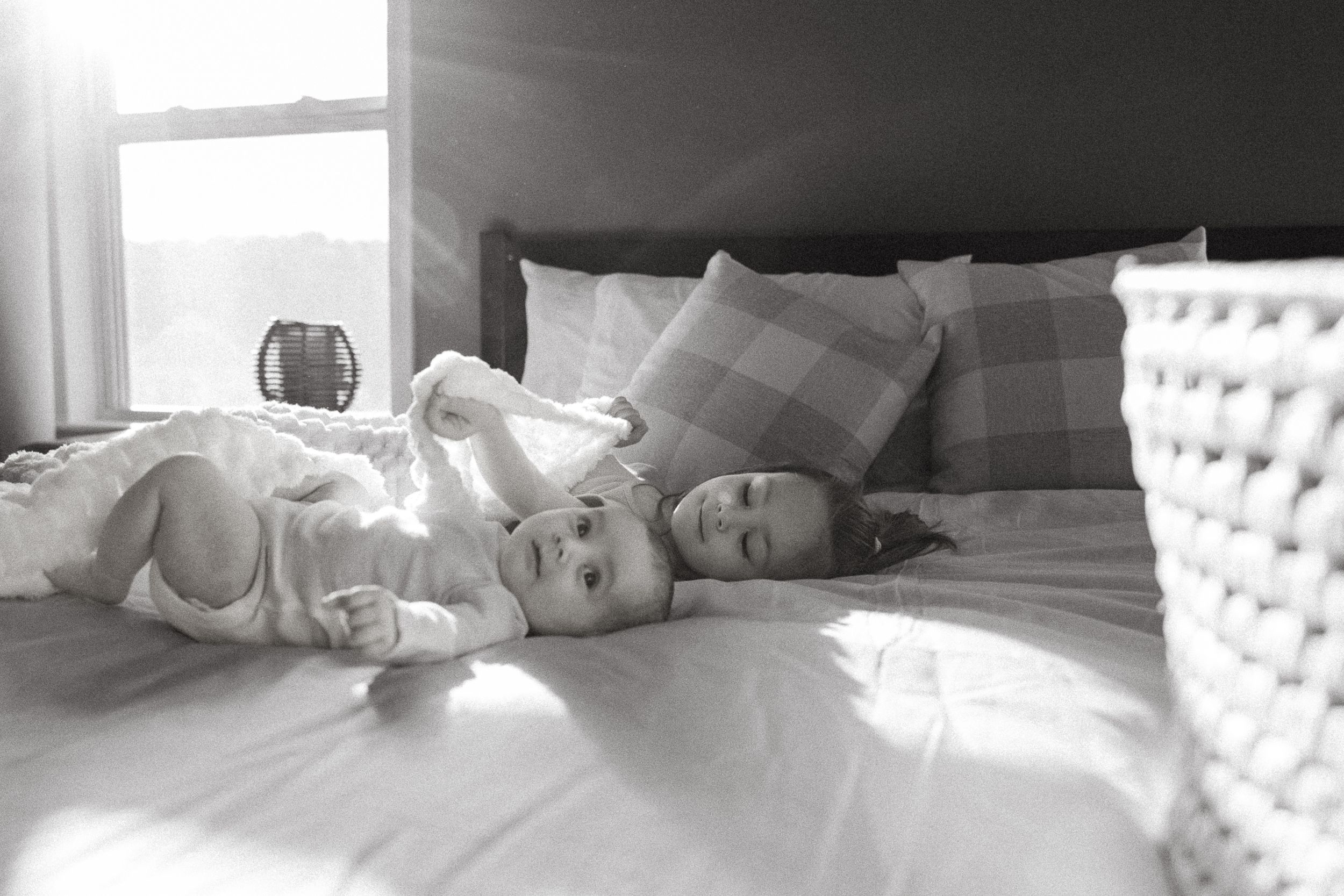 A black and white photograph shows light streaming through a window onto a cozy bed with white bedding and pillows.