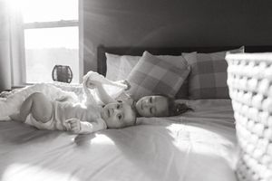 A black and white photograph shows light streaming through a window onto a cozy bed with white bedding and pillows.