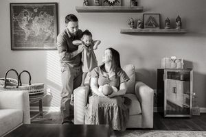A tender black and white family moment captured in a cozy living room with decorative shelves and artwork on the wall.