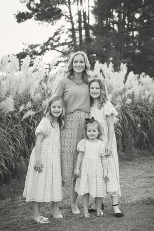 A black and white portrait of a family standing together in front of pampas grass and trees.