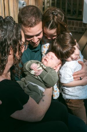 Family gathered closely admiring a sleeping newborn baby wrapped in a green blanket, sharing a tender moment together.