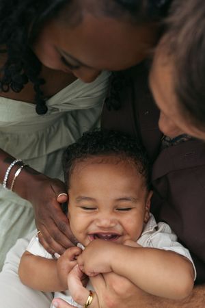 A close-up candid shot of a laughing baby being held by loving hands wearing bracelets.