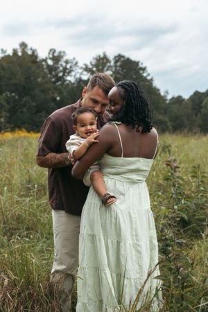 A tender family embrace in a sunlit meadow with tall grass and wildflowers.