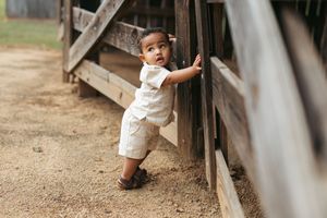 A child in white clothing plays near a weathered wooden fence in an outdoor setting.
