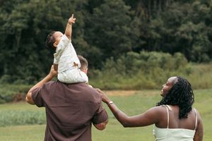 A couple in brown and white attire dance together in a grassy field during what appears to be a wedding celebration.