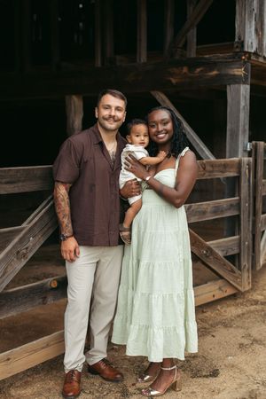 A family poses together in front of a rustic wooden barn wearing casual attire in earth tones.