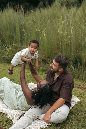 A loving family moment captured on a white blanket in a grassy field during a summer day.