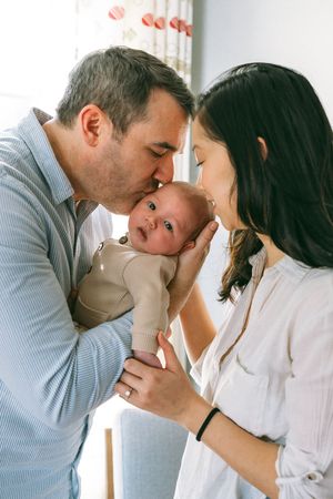 A loving couple sharing a tender moment with their newborn baby in a bright indoor setting.