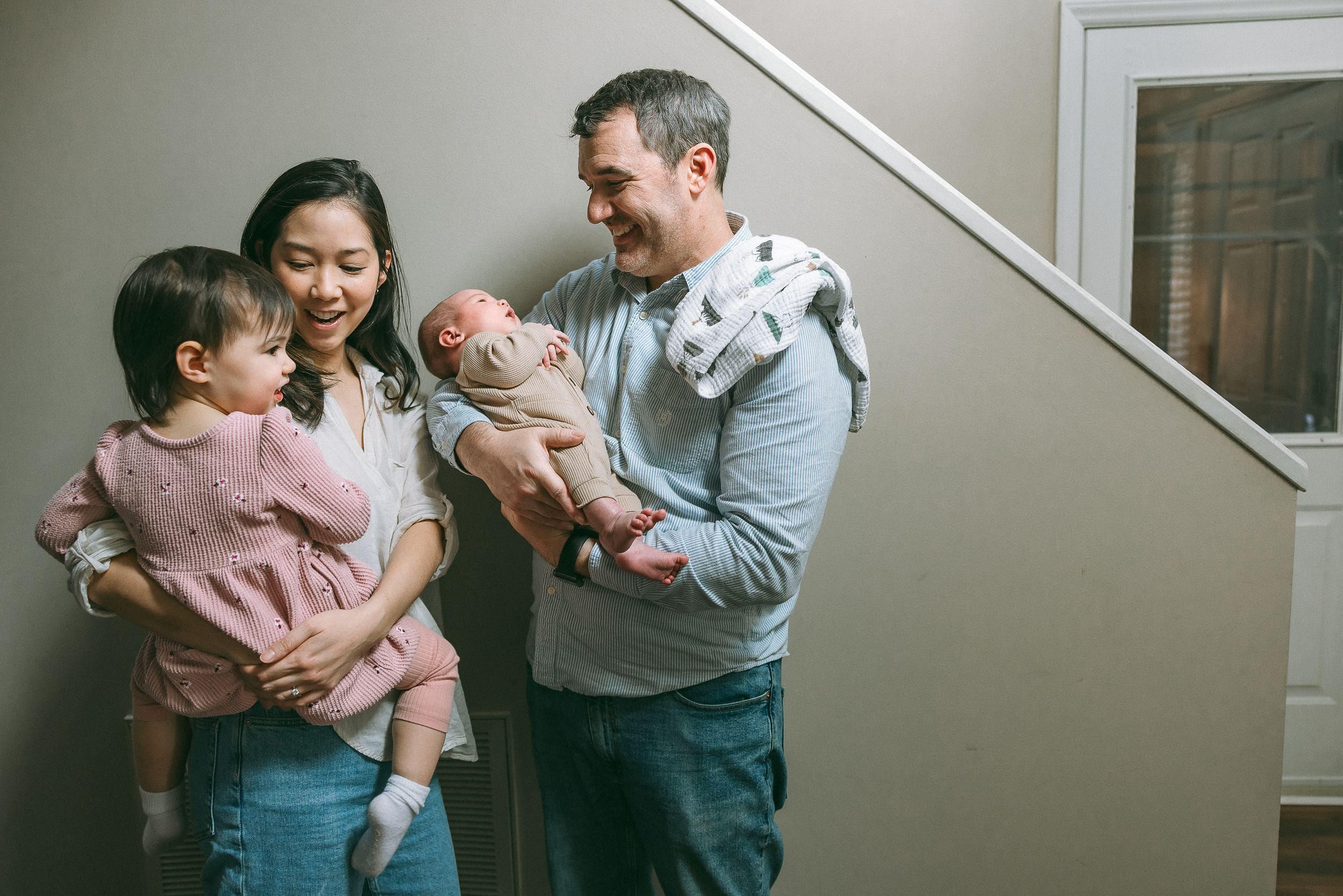 Happy family of four stands together in their home near a staircase.