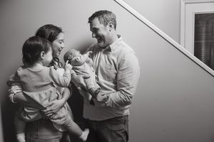 A black and white candid photograph of parents sharing a joyful moment with their two young children on a staircase.
