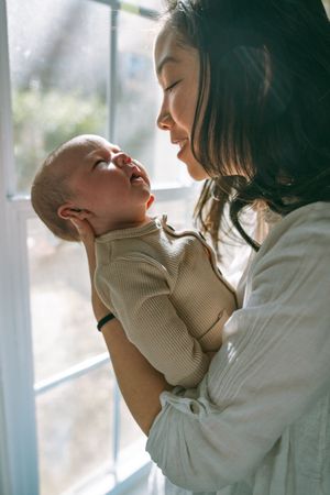 A tender moment between a baby in ribbed sweater and parent near a sunlit window.