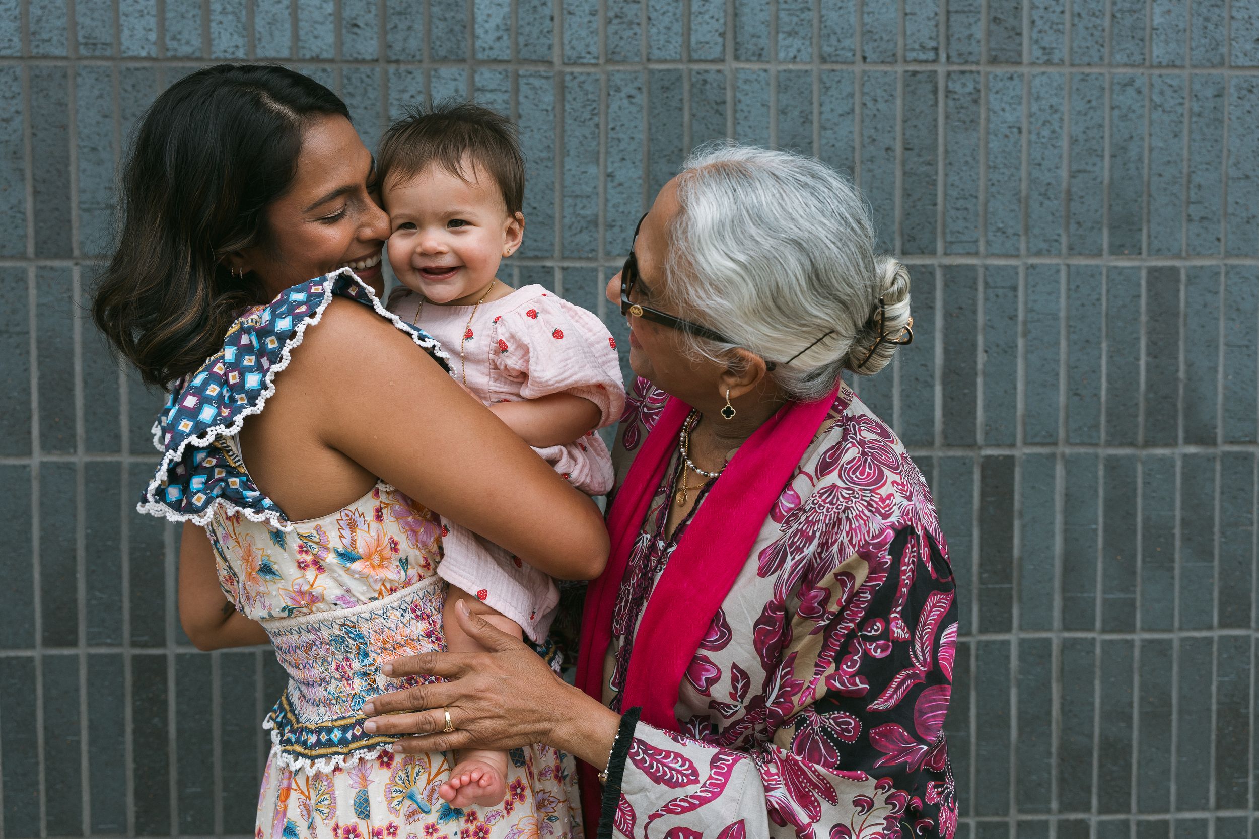 Three generations of women share a joyful moment, with a mother holding a smiling baby while an older woman looks on.