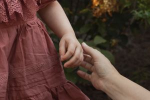A close-up of two hands touching tenderly against a background of pink fabric.