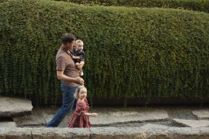 A family walks together along a path beside a tall green hedge.