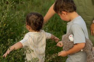 Children walking through tall grass holding stuffed animals.