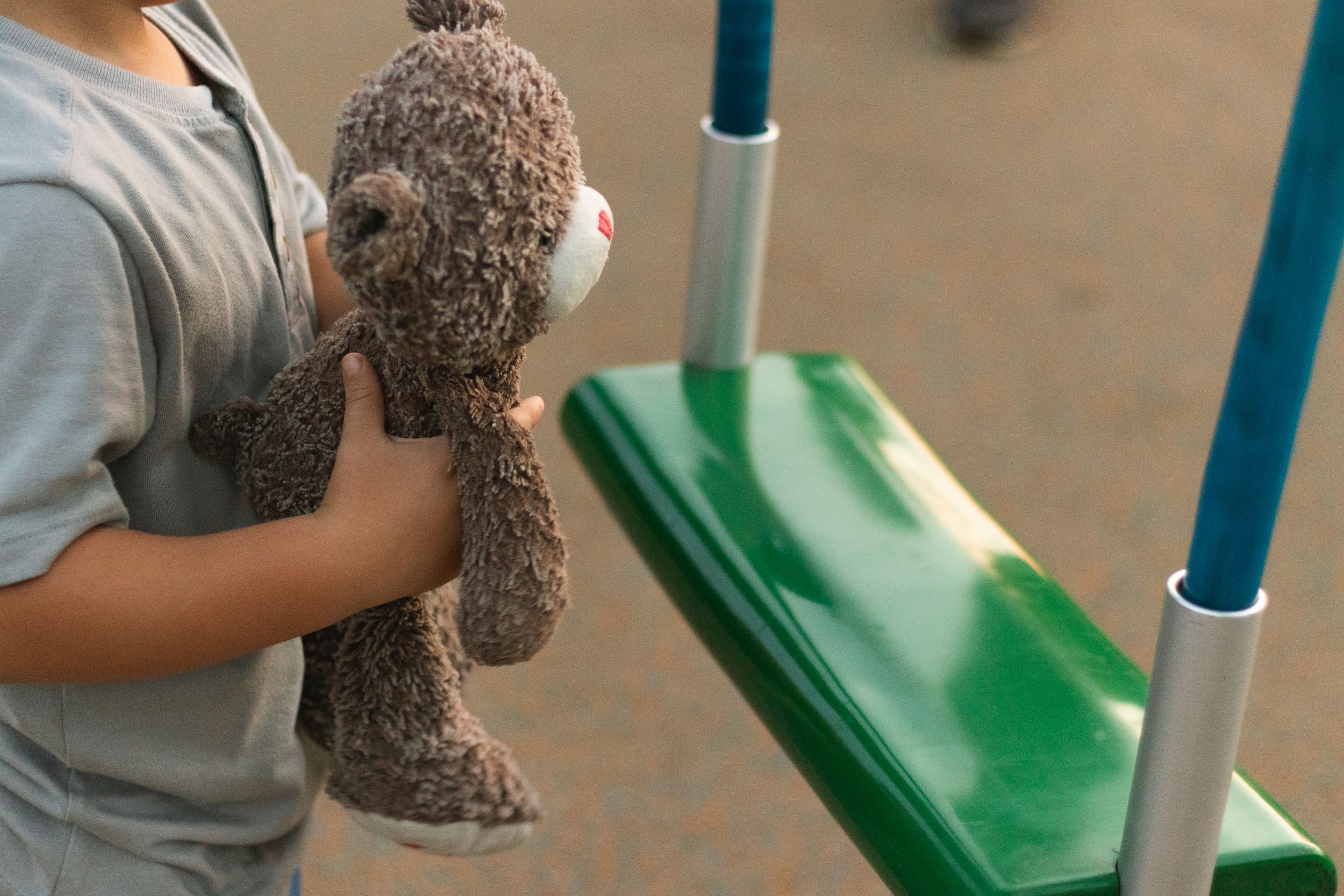 Child holding a plush teddy bear near playground equipment.