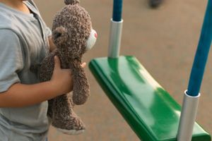 Child holding a plush teddy bear near playground equipment.
