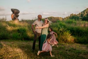 A family enjoying a playful moment together in a grassy field during golden hour.