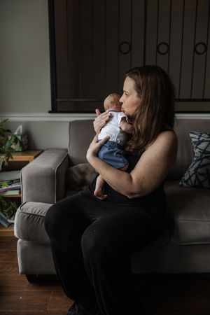 Parent and infant share tender quiet moments together on a grey couch in dim natural lighting.
