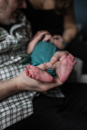 Close-up photo of tiny newborn baby feet being gently cradled in adult hands against plaid fabric background.