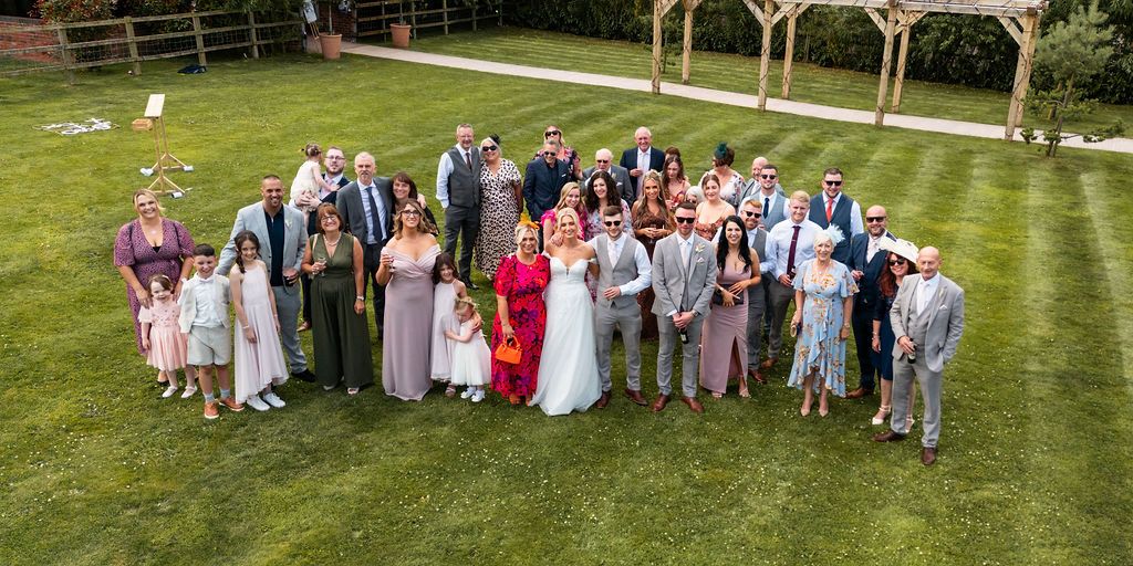 Group photo of the bride, groom, and wedding guests gathered on the lawn at Coton House Farm